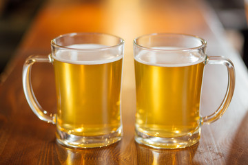 Two transparent cups of light beer on a wooden table in pub.