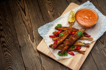 Roasted capelins with lemon and dip sauce on a wooden plate