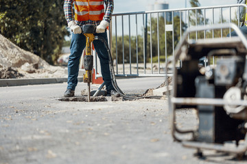 Craftsman in uniform with drill repairing asphalt during roadwork
