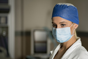 Young blonde nurse in ER room in a surgical mask and surgical cap