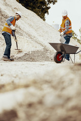 Low angle of workers with shovels pouring sand into the wheelbarrow