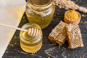 Beautiful transparent honey in bank, honeycombs and pollen on a wooden table. It can be used as a background