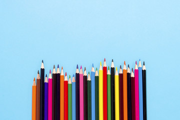 Color pencils laid out in the form of a wave on a blue background. Flat lay, top view
