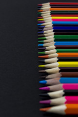 Colored pencils lined in a row on a black background background