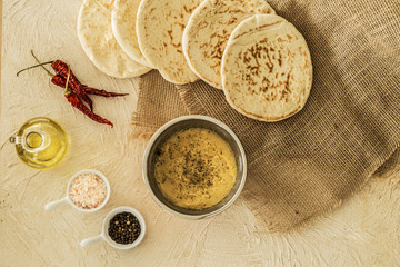 Pita bread, hummus in a bowl, salt, pepper, olive oil and red chili peppers on a table