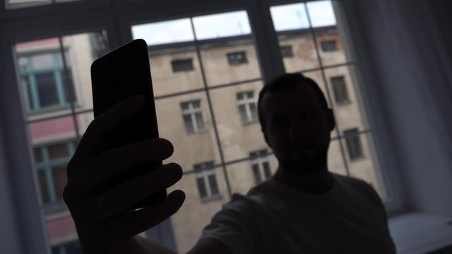Man taking selfie picture silhouette by the window at home