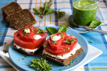 Gesundes Frühstück mit Bauernbrot-
scheiben, Streichkäse, Tomaten und einem Glas Gemüe-Smoothie