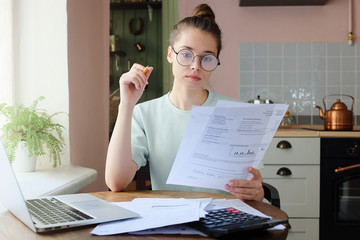 Portrait of young woman, sitting at kitchen table, filling application form, calculating expences,...