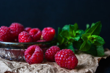 Raspberries in a glass plate with mint leaves on a black background.