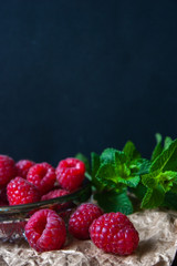 Raspberries in a glass plate with mint leaves on a black background.