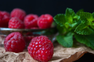 Raspberries in a glass plate with mint leaves on a black background.