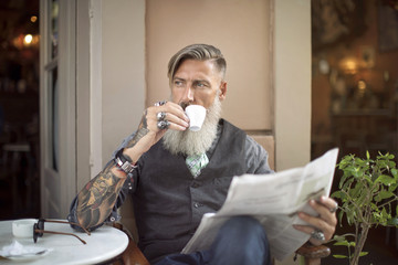 Attraktiver Mann sitzt in einer Coffeeshop, trinkt  Kaffee und liest  Zeitung