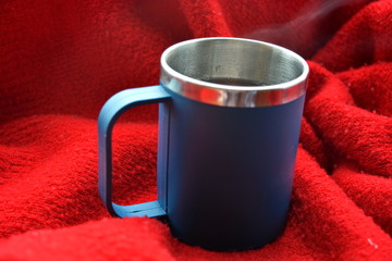 Blue tea cup with handle with a hot drink of steam on the background of red plaid