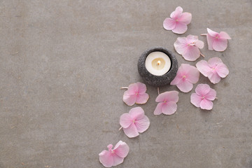 Pile of Pink hydrangea petals with candle in stone bowl on gray background