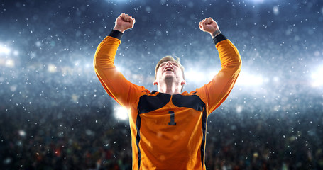 Soccer player celebrates a victory on the professional stadium while it’s snowing.
