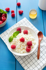 Tvorog, cottage cheese or ricotta with raspberries in bowl on blue background, top view