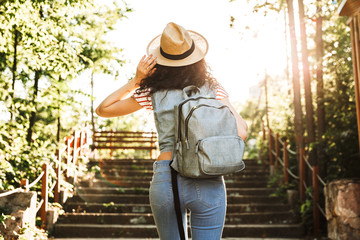 Photo from back of attractive woman 18-20 wearing summer clothes and straw hat, walking up stairs...