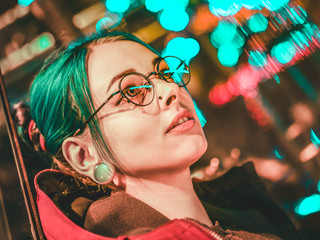 Portrait of young pretty girl with unusual hairstyle lying on glass wall which glowing colorful...