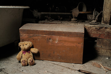 Childs teddy bear and an old chest in the dusty attic space of an old house