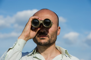 bearded man detective looks through binoculars in the distance and watches.