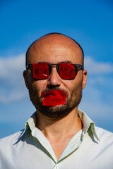 Conceptual portrait of a businessman in a goggle with glasses and mouth against a blue sky.