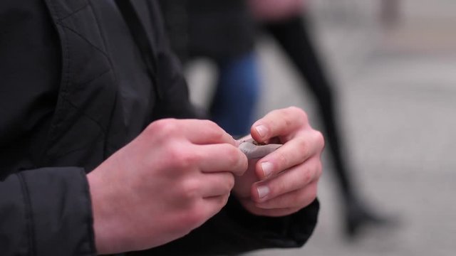 Teenager guy makes a hand-made cigarette on a street wraps tobacco in paper