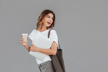 Image of young brunette woman 20s smiling and looking backside at copyspace while standing against...