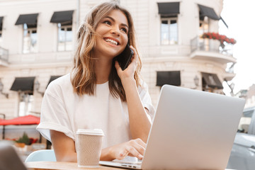 Portrait of happy young woman sitting at table in cafe outdoor on summer day, and and having mobile...