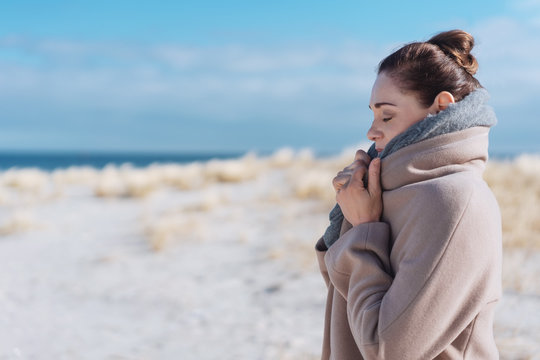 Frau steht im winter am strand und kuschelt sich in ihren mantel