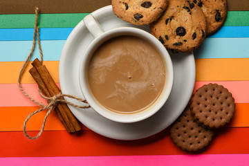 Drink with caffeine or cocoa with milk. Coffee on colorful positive background, top view. Coffee break concept. Cup of coffee with milk or cappuccino with cookies and cinnamon on colorful background
