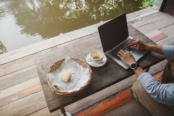 Professional web designer using laptop with mock up screen for creating project. Top view of designer making  web page on laptop computer in co-working space near pond.
