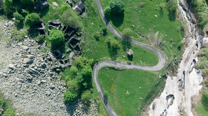 Aerial: top down view tailspin over winding mountain road on the Italian Alps, crossing green meadow and pasture in alpine valley, adventure road trip in summer.
