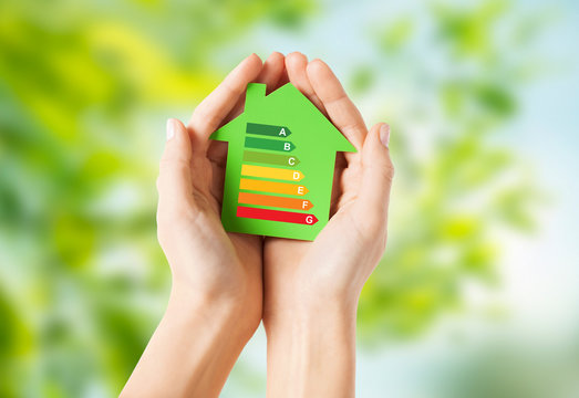 efficiency  and home concept - closeup of female hands holding green paper house with energy saving rating over natural background
