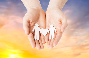 lgbt and gay concept - hands holding paper male couple pictogram with heart over evening sky...