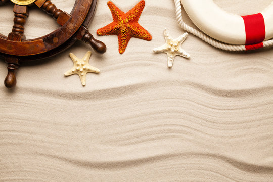 Beach background - ship's steering wheel, lifebuoy and starfish on sand