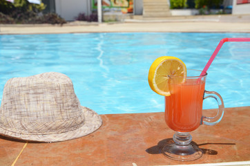 Fresh glass of water-melon smoothie drink with sunglasses, straw hat and slippers on border of a swimming pool - holiday tropical concept
