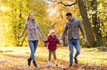 Naklejka premium family, season and people concept - happy mother, father and little daughter walking at autumn park