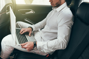 Confident young businessman working on his laptop while sitting in the car