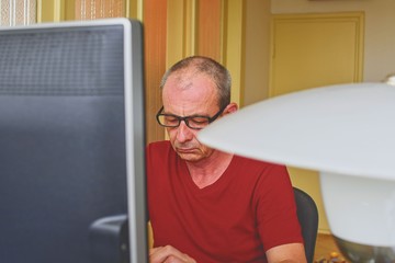 Middle aged man with glasses sitting at desk. Mature man using Personal computer. Senior concept