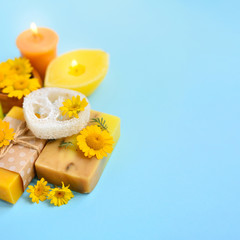 Spa composition with natural soap, candles, aroma oil in bottles and flowers on blue background with empty space for text