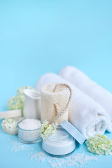 Spa composition with cream, salt, towel and flowers on a blue background with empty space for text.