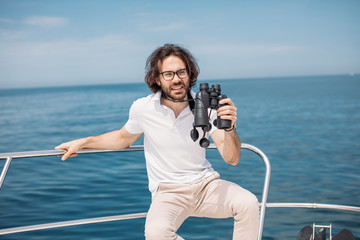 European bearded yachtsman looking through binoculars from the boat in search of transatlantic...