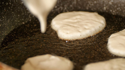 Closeup view pouring fresh white pancake dough mixture into preheat cast iron pan with vegetable oil at home