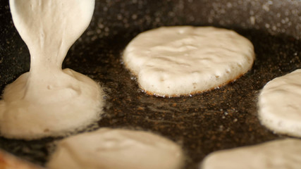 Closeup view pouring fresh white pancake dough mixture into preheat cast iron pan with vegetable oil at home