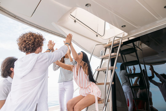Happy cheerful young friends giving a high five slapping each others hand in congratulations, enjoying marine cruise on comfortable yacht