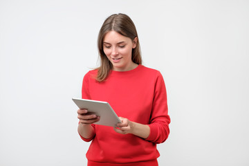 Naklejka premium Elegant young woman in red sweater using tablet, looking at screen