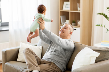 family, fatherhood and people concept - happy father with little baby boy sitting on sofa at home