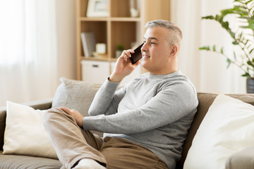 Fototapeta premium technology, people and communication concept - happy man calling on smartphone at home