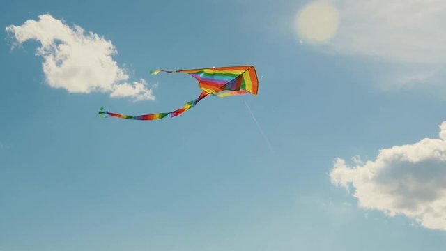 A colored kite in the blue sky. Slowed-down shooting of a kite developing against a blue sky and white clouds