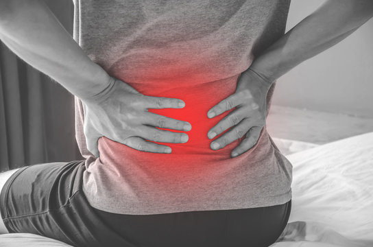 Man suffering from back pain at home in the bedroom. Uncomfortable mattress and pillow causes back pain.